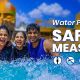 Four friends laughing and enjoying the waves in the crystal-clear pool at Wet’nJoy Lonavala, with water park safety rules icons displayed on the banner to highlight the park's strict safety standards.